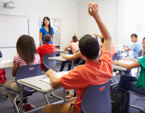 Child with hand up in a classroom